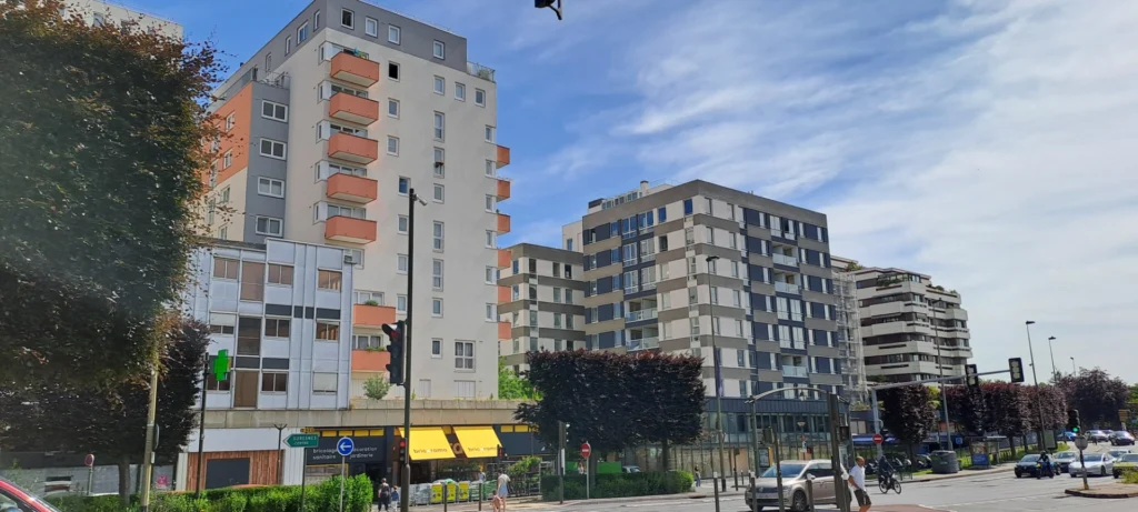 Residential apartment buildings on a city street, with orange balconies, under a blue sky
